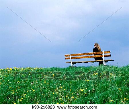 Stock Image - Woman sitting on bench during upcoming rain. Altes Land, Lower Saxonia. Germany. Fotosearch
