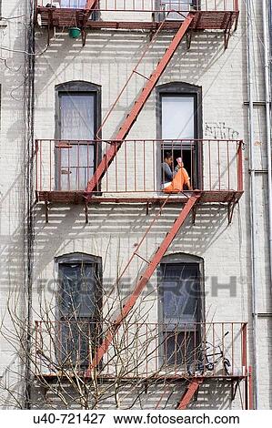 Stock Photo - Woman sitting on fire escape, NYC, USA. Fotosearch