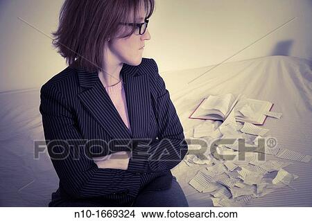Woman sitting on her bed next to a book with ripped-up pages View Large Photo Image Picture - Woman sitting on her bed next to a book with ripped-up pages. Fotosearch