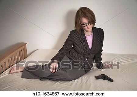Woman sitting on her bed, next to a handgun View Large Photo Image Stock Photo - Woman sitting on her bed, next to a handgun. Fotosearch