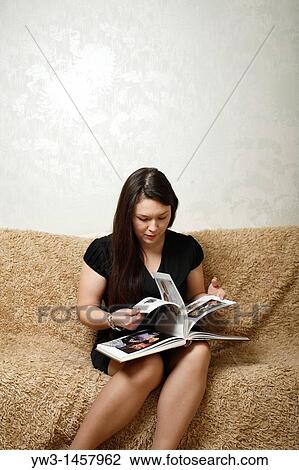 Woman sitting on sofa, looking at book View Large Photo Image Stock Image - Woman sitting on sofa, looking at book. Fotosearch