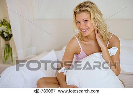 Stock Photo - Woman sitting on the bed looking at camera. Fotosearch