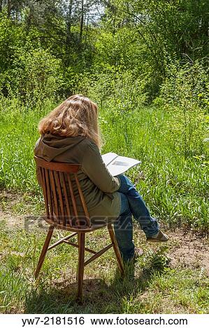 Woman sitting outdoors on a chair and reading. View Large Photo Image Stock Photograph - Woman sitting outdoors on a chair and reading.. Fotosearch