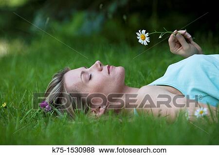 Stock Photo - Woman smelling a daisy on lawn. Fotosearch