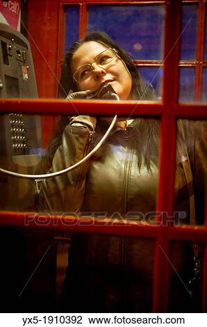Stock Image - Woman speaking on the phone in a telephone booth in London. Fotosearch
