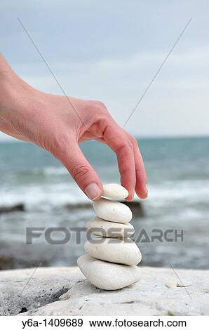 Stock Photo - Woman stacking stones on beach. Fotosearch
