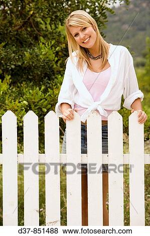 Woman standing behind the fence in the garden smiling View Large Photo Image Stock Photo - Woman standing behind the fence in the garden smiling. Fotosearch