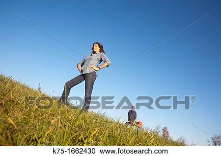 Woman standing in field with man in background View Large Photo Image Stock Image - Woman standing in field with man in background. Fotosearch