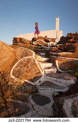 Picture - Woman standing in front of a chapel at the top of the hill in Chora, Ios, Cyclades Islands, Greek Islands, Greece, Europe.. Fotosearch