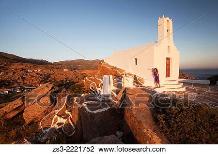 Stock Image - Woman standing in front of a chapel at the top of the hill in Chora, Ios, Cyclades Islands, Greek Islands, Greece, Europe.. Fotosearch