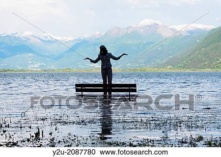 Woman standing on a bench in a flooding alpine lake maggiore, with snow-capped mountain in background in ticino switzerland View Large Photo Image Stock Image - Woman standing on a bench in a flooding alpine lake maggiore, with snow-capped mountain in background in ticino switzerland. Fotosearch