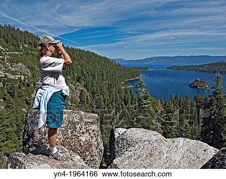 Woman standing on large rocks looking through binoculars at Lake Tahoe. View Large Photo Image Stock Photograph - Woman standing on large rocks looking through binoculars at Lake Tahoe.. Fotosearch