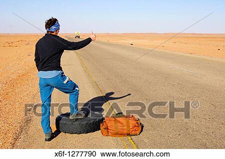 Woman standing with a travelling bag next to a flat tyre at the edge of a lonly country road trying to stop a car for help, Al Awaynat Libya View Large Photo Image Stock Image - Woman standing with a travelling bag next to a flat tyre at the edge of a lonly country road trying to stop a car for help, Al Awaynat Libya. Fotosearch