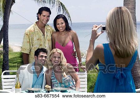 Picture - Woman taking a group photo of people dining at the beach. Fotosearch