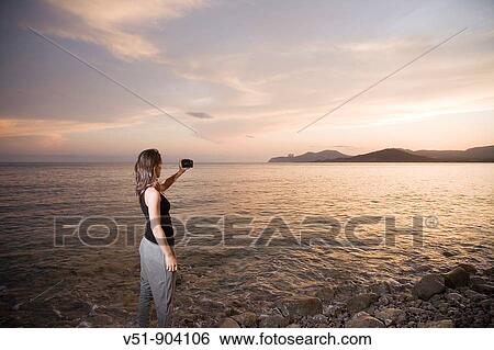 Stock Photograph - Woman taking a photograph at sunset. Fotosearch