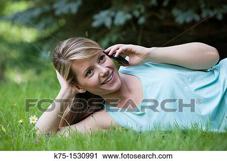 Stock Image - Woman talking on cell phone while lying on lawn. Fotosearch