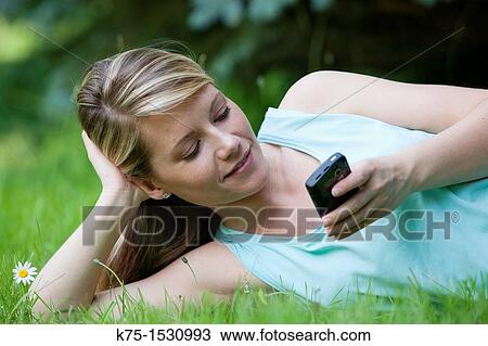 Stock Image - Woman texting on her cell phone while relaxing on the lawn. Fotosearch