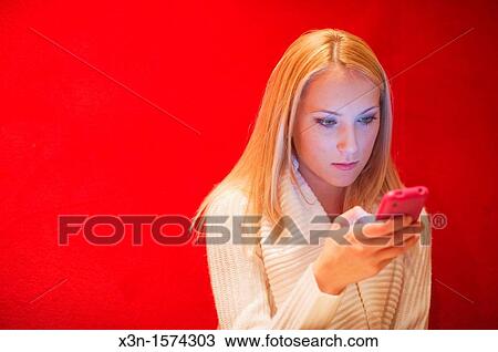 Stock Image - Woman texting with iphone against red wall. Fotosearch