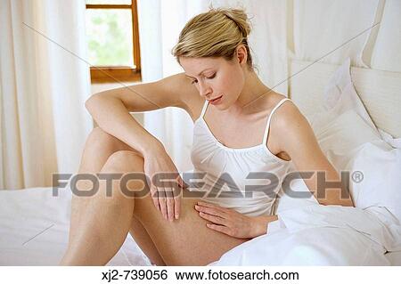 Stock Photograph - Woman touching her legs on the bed. Fotosearch