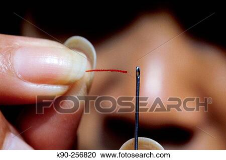 Woman tries to put a threat through the hole of a needle View Large Photo Image Stock Image - Woman tries to put a threat through the hole of a needle. Fotosearch