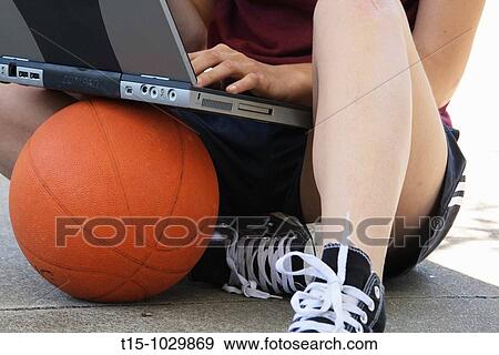 Stock Photo - woman using a laptop sitting on top of a basketball. Fotosearch