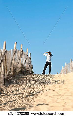 Stock Photo - Woman views the beach from a dune path. Fotosearch