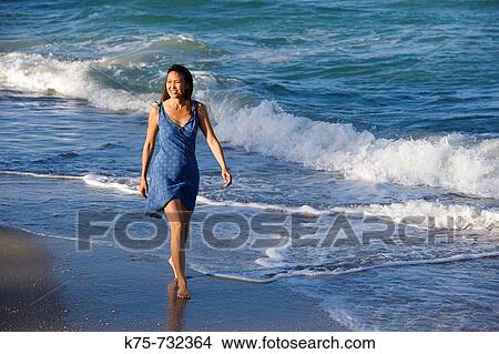 Picture - woman walking along surf. Fotosearch