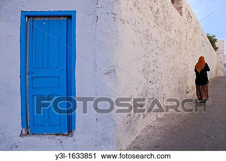 Woman walking by a white limed wall and blue door, Mahdia, Tunisia View Large Photo Image Stock Image - Woman walking by a white limed wall and blue door, Mahdia, Tunisia. Fotosearch