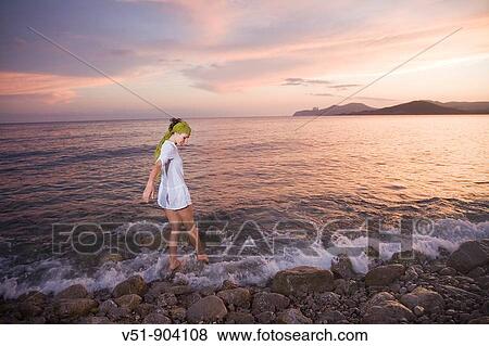 Stock Photo - Woman walking on the beach at sunset. Fotosearch