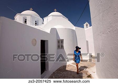 Stock Photography - Woman walking through the alley in Chora with the church in the background, Amorgos, Cyclades Islands, Greek Islands, Greece, Europe.. Fotosearch