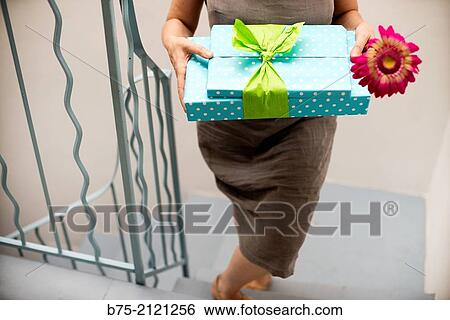 Stock Photograph - Woman walking up stairs giving some gift packs and a flower. Fotosearch