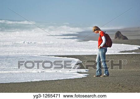 Stock Image - woman watching incoming waves on empty beach. Fotosearch