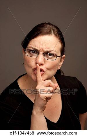 Woman wearing glasses with her finger to her lips calling for silence quiet no talking View Large Photo Image Stock Photo - Woman wearing glasses with her finger to her lips calling for silence quiet no talking. Fotosearch