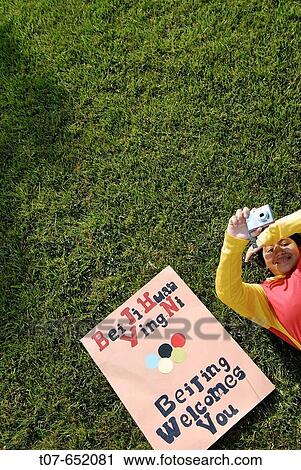 Stock Image - Woman wearing the Chinese Olympic Uniform colors The poster reads in simplified Chinese (Mandarin)? Beijing Welcomes You? - Bei Jing Huan Ying Ni or Beijing huanying ni. The names bring forth China's gradual changes and development The New China.. Fotosearch