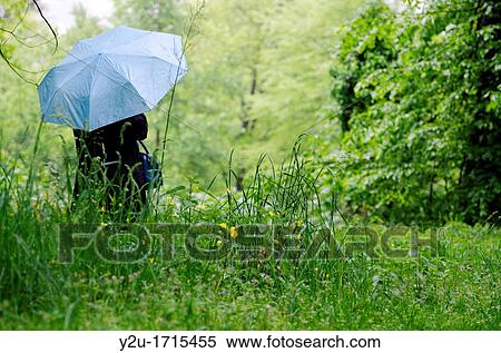 Woman with a blue umbrella on the wet green field with grass and flowers View Large Photo Image Stock Photography - Woman with a blue umbrella on the wet green field with grass and flowers. Fotosearch
