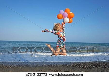 Stock Image - Woman with balloons jumping in the beach. Fotosearch