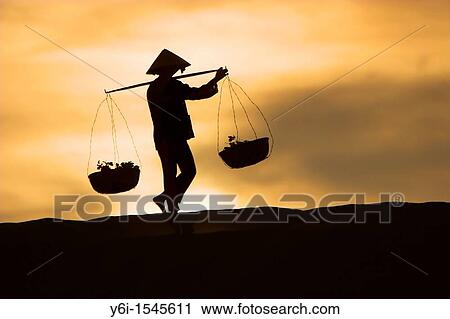 Woman with conical hat carries pannier baskets in sunrise along crest of sand dunes near Mui Ne Vietnam View Large Photo Image Stock Image - Woman with conical hat carries pannier baskets in sunrise along crest of sand dunes near Mui Ne Vietnam. Fotosearch