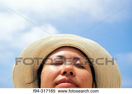 Stock Photography - Woman with round hat enjoying the sunshine with a blue sky in the background. Fotosearch