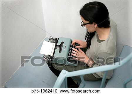 Stock Image - Woman with typewriter sitting on the steps. Fotosearch