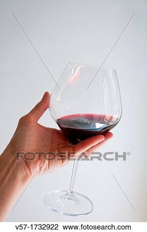 Stock Image - Woman's hand holding a glass of red wine, tasting it. Fotosearch
