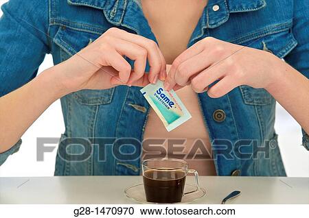 Stock Image - woman's hands putting sugar sweetener into a cup of coffee. Fotosearch
