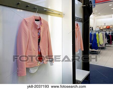 Stock Image - Woman`s jacket hanging in dressing cabin, reflection, mirror. Retail store, shop, shopping.. Fotosearch