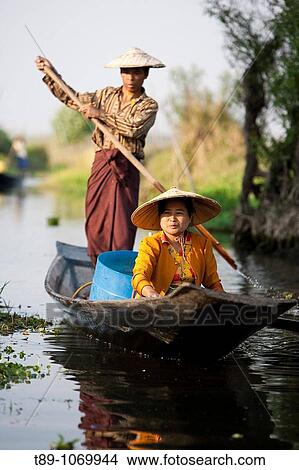 Picture - Women going to market by boat on Lake Inle with a typical Intha village of houses on stilts in the background.. Fotosearch