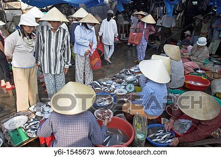 Stock Image - Women in conical hats buy and ssell fish at riverside market Hoi An historic town mid Vietnam. Fotosearch