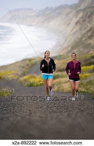 Stock Image - WOMEN RUNNING ON TRAIL ALONG THE OCEAN. Fotosearch
