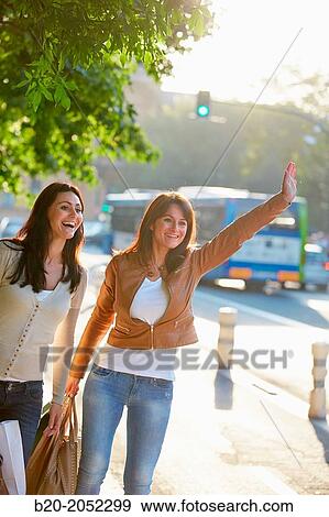 Stock Photo - Women sisters 35 and 40 years hailing a cab. Shopping on the street. Donostia. San Sebastian. Gipuzkoa. Basque Country. Spain.. Fotosearch