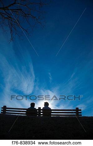 Women talking under whispy clouds while sitting on park bench View Large Photo Image Picture - Women talking under whispy clouds while sitting on park bench. Fotosearch