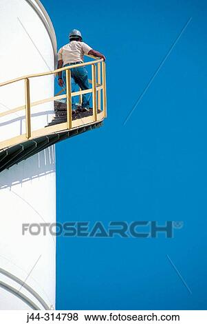 Stock Photo - Worker ascending staircase on chemical storage tank. Fotosearch