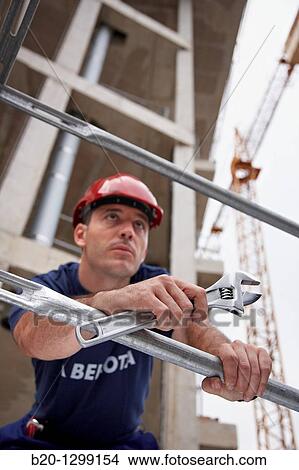 Picture - Worker holding adjustable spanner in a construction site. Fotosearch