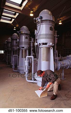 Stock Photography - Worker in pump room checking plans at water treatment plant. Fotosearch